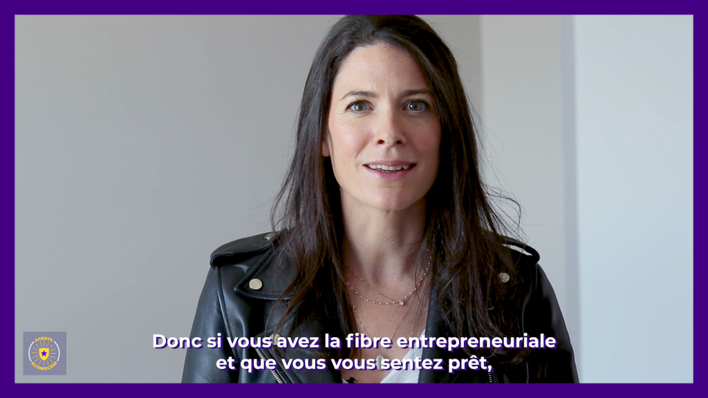 capture d'écran de fil institutionel. Une femme de 45 ans brune qui s'adresse à la caméra avec un sourire. Elle est habillée avec un tshirt et un perfecto en cuir noir. le mur derière elle est blanc.